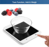 Digital kitchen scale with a glass bowl and hand pressing a button, surrounded by berries.